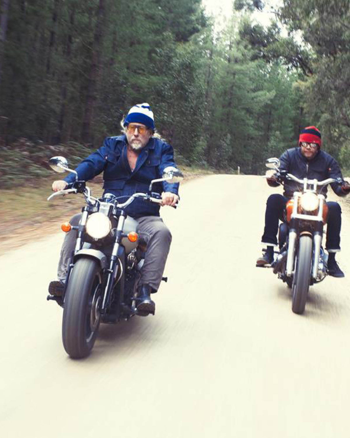 Two men riding motorcycles wearing fallen BROKEN street fisherman beanies drive along a dirt road in the Victorian forest