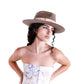 A woman models The Zephyr felt hat in vintage brown against a white backdrop. Styled with a strapless floral dress, the image highlights the hat’s bold brim, frayed cotton band, and hand-shaped crown. This wide-brimmed wool hat offers both elegance and function, making it the perfect accessory for summer adventures or road trips. FallenBROKENstreet signature style with vintage flair.

