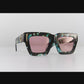 Studio video still showing The Mischief sunglasses on a shelf with pink lenses and galaxy frame in crisp lighting. Chain attachments visible.

