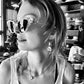 Model wearing The Astral Plane – Skywalker/Amber sunglasses, featuring a bold cat-eye shape with clear acetate frame. Image is in black and white with reflective lens highlights, showcasing statement style and gold detailing.

