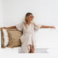 Model lounging in a striped playsuit on a white couch with the sunglasses styled in an indoor lifestyle setting

