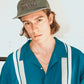 Model in teal bowling shirt and Dope Lemon dad cap looking to the side against a white background.


