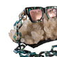 Close-up of The Mischief – Galaxy/Pink sunglasses with attached black chain on a bed of raw crystals. Highlights chain compatibility and styling flexibility.

