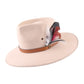The Drift hat in a soft blush tone with an oversized feather and leather band, shown on white background, exudes individuality and character.

