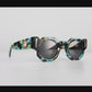Video of Close-up of THE COSMOS – Galaxy/Black sunglasses hanging off quartz crystal, showcasing chain compatibility, acetate pattern, and gold hardware.

