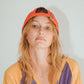 Woman in orange and purple tee facing forward, wearing the cap backward.

