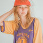 Woman wearing red Stingray Pete cap backward with hand resting on head.

