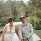 Couple seated outdoors wearing matching sunglasses and neutral-toned outfits. Captures a relaxed, stylish moment in natural light.

