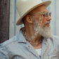 Older male model wears The Mischief – Skywalker/Amber sunglasses with white hat and button-up shirt. Styled in natural light with a relaxed, vintage feel.

