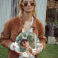 Fashion photo of model in The Cosmos – Skywalker/Amber sunglasses styled with shearling jacket and holding a ceramic sculpture. Fall tones complement amber lenses, delivering peak retro mood.