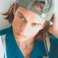 Male model wearing Dope Lemon cap backwards, looking into camera in a teal striped shirt.

